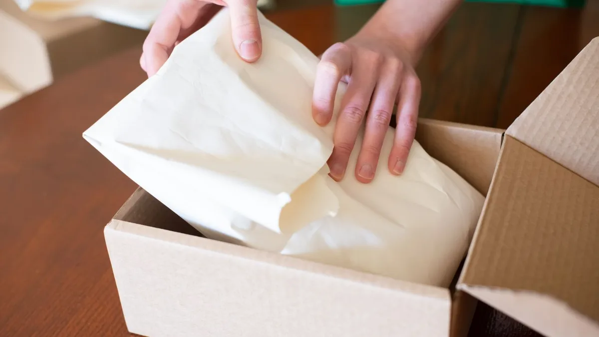 Hands packing an order with paper cushioning into a corrugated shipping box